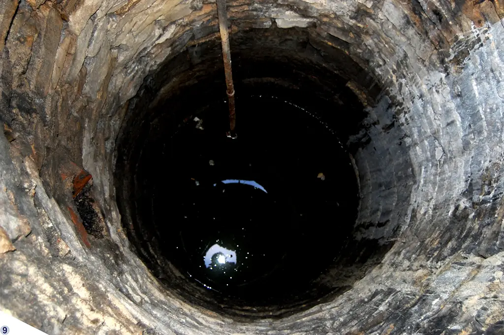 Blick in einen tiefen runden Brunnen der mit Wasser gefüllt ist.