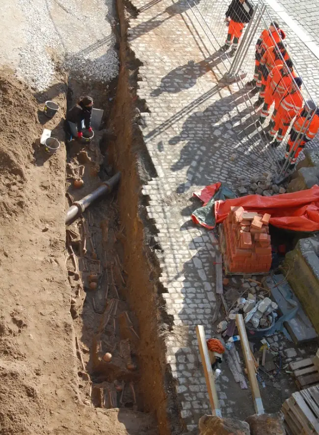 Bauarbeiter sehen in einen Graben auf die restlichen Gebeine des aufgelösten Beinhauses. Die Ausgrabung erfolgte durch Dr. Magnus Wintergerst im Jahr 2011/2022